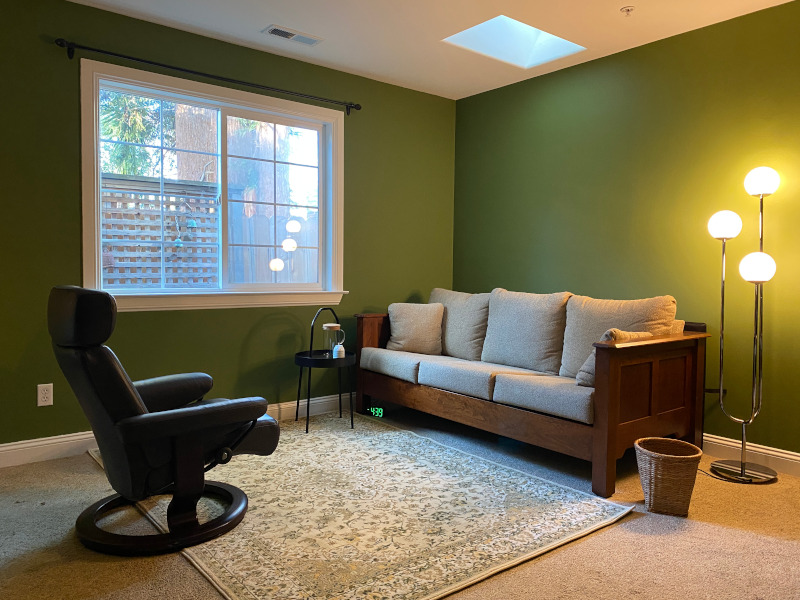 A photograph of a room with green walls, couch, and therapist chair.